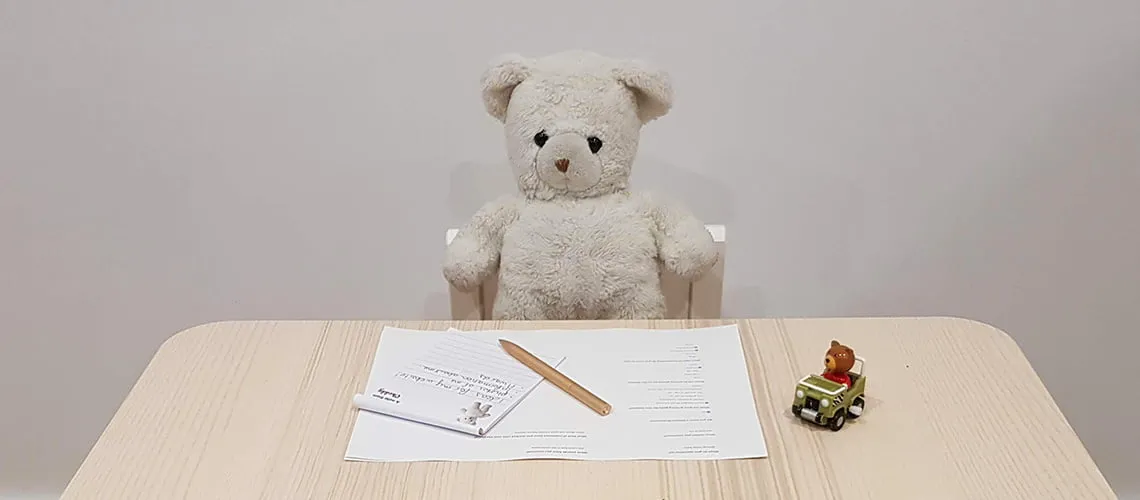 Teddy bear behind desk with paper and toy car.